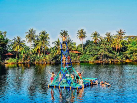 Group of Young Travellers on large River Raft with Diving platform with Palm Trees and blue Sky