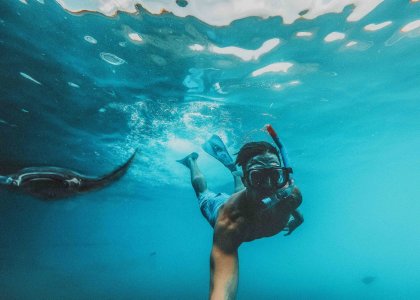 An underwater selfie of someone snorkelling with Manta rays in the bright blue ocean in the Maldives 